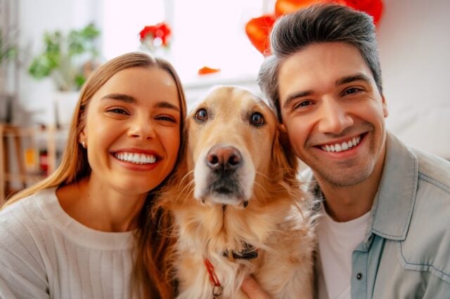 Smiling,Young,Couple,Posing,Closely,With,Their,Golden,Retriever,At Why Dogs MIrror Their Owner's Energy and Personality Featured Image